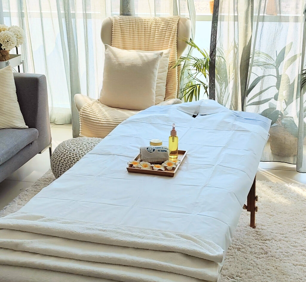 Massage table with fresh white linens set up in a bright living room.